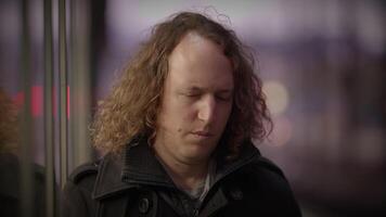 A man with long curly hair sits on a bus, eyes closed video