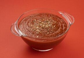 Bowl of tomato soup isolated on red background photo