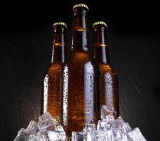 frío cerveza con agua gotas, cerveza botellas con hielo cubitos foto