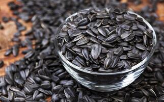 Bowl full of black sunflower seeds on wooden background with copy space photo