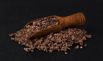 Grated chocolate in wooden scoop isolated on black background, closeup photo