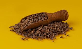 Grated chocolate. Pile of ground chocolate in wooden scoop isolated on yellow color background, closeup photo