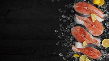 Fresh salmon steaks on black background, piece of chilled red fish on ice, top view photo