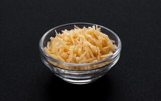 Grated parmesan cheese in glass bowl, black background photo