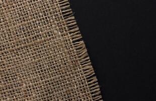 Old burlap fabric napkin on black background, top view photo
