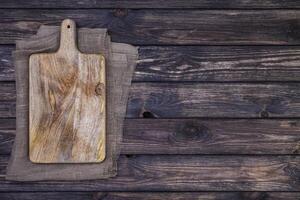Old cutting board on dark wooden table. Top view. Copy space photo