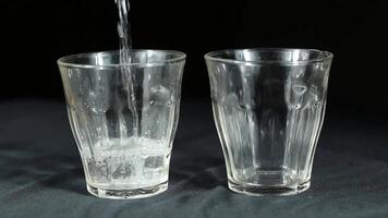 Gießen Wasser in zwei transparent Brille auf ein schwarz Hintergrund video