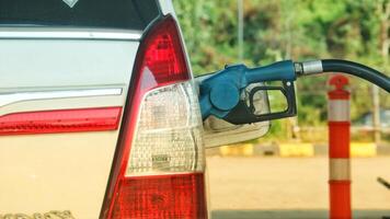 A white car is filling its gas tank at a gas station. The nozzle is blue. photo