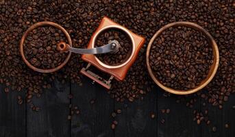 Ground coffee, coffee mill, bowl of roasted coffee beans on black wooden background, top view photo