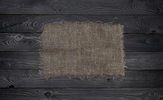 Old burlap fabric napkin on black wooden background, top view photo