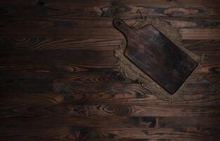 Cutting board with burlap napkin on brown wooden background, top view photo