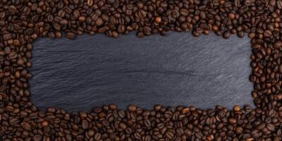 marco hecho de granos de café tostados en la mesa negra, vista superior foto