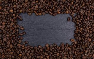 marco hecho de granos de café tostados en la mesa negra, vista superior foto
