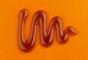 Caramel sauce on orange color background, top view photo