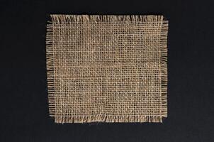 Old burlap fabric napkin on black background, top view photo