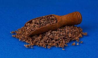 Grated chocolate in wooden scoop isolated on blue color background, closeup photo