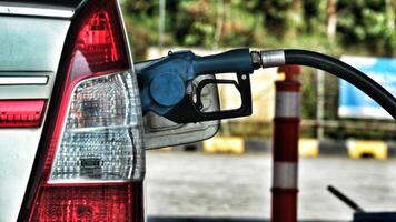 A white car is filling its gas tank at a gas station. The nozzle is blue. photo