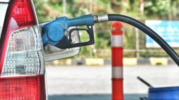 A white car is filling its gas tank at a gas station. The nozzle is blue. photo