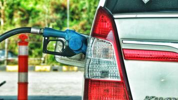 A white car is filling its gas tank at a gas station. The nozzle is blue. photo