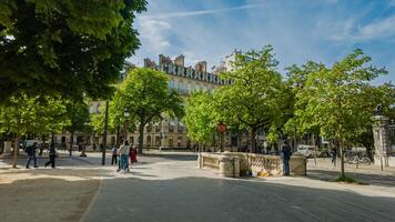 Springtime in Paris, France, showcasing pedestrians enjoying a sunny afternoon in a tree lined public square, captured on April 14th, 2024, ideal for travel and leisure themes photo