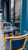 Empty blue wicker chairs at a Parisian sidewalk cafe with a reflective metal table, evoking concepts of travel, European culture, and leisure photo