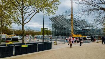 visitantes caminando por el en marcha construcción de un moderno estructura en París, Francia, debajo primavera floración en abril 14, 2024, reflejando urbano desarrollo y turismo foto