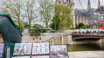 Colorful Parisian street art for sale on the Seine Riverbank with Notre Dame Cathedral restoration in background, Paris, France, April 14th, 2024, springtime concept photo