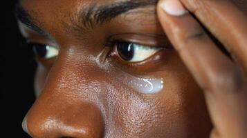 Using his ring finger he gently taps an eye cream under and around his eye area photo