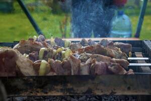 Cooking kebabs on a grill with smoke. Fresh brown BBQ meat cooked on an outdoor grill photo