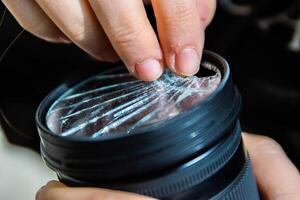 Photographer removing broken pieces of glass out of DSLR photo camera lens filter after if fall down onto the floor. Close up. Destroyed cracked glass of photo-filter. Macro. Top view. Selective focus