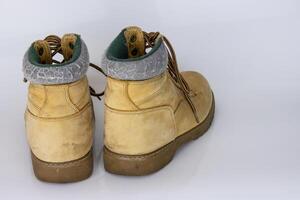 Pair of worn old yellow hiking trekking lace boots Isolated on white glossy surface with beautiful reflection effect. Second hand tourist walking shoes. Back view. Copy Space. White background. photo