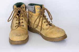 Pair of worn old yellow hiking trekking lace boots Isolated on white glossy surface with beautiful reflection effect. Second hand tourist walking shoes. Side view. Copy Space. White background. photo