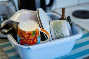 Clean dishes - cups, plates, bowls, cooking pot are getting dry in the broken blue washbowl at the camping kitchen. Drying utensils on the kitchen counter. selective focus photo