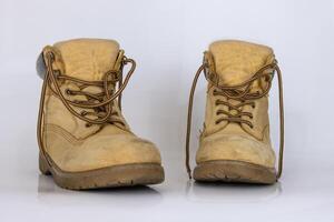 Pair of worn old yellow hiking trekking lace boots Isolated on white glossy surface with beautiful reflection effect. Second hand tourist walking shoes. Side view. Copy Space. White background. photo