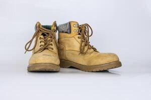 Pair of worn old yellow hiking trekking lace boots Isolated on white glossy surface with beautiful reflection effect. Second hand tourist walking shoes. Side view. Copy Space. White background. photo