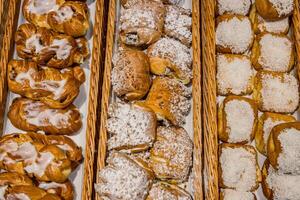 A lot of sweet pastries in baskets on the counter in the food store. Bakery on the buffet table. Business breakfasts and catering at events. Various bread type on shelf. Close-up. Selective focus. photo