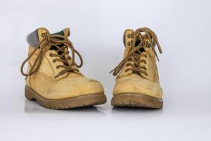 Pair of worn old yellow hiking trekking lace boots Isolated on white glossy surface with beautiful reflection effect. Second hand tourist walking shoes. Side view. Copy Space. White background. photo