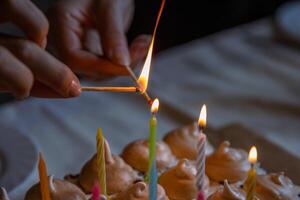 Hands of two people lighting colorful candles on the large homemade chocolate cake, decorated with meringues and whipped cream. Celebration party concept. Close-up. Selective focus. photo