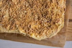 Backing process. Closeup of Puff pastry layers of the French Napoleon cake laying on the backing paper on the wooden cutting board. French pastry with custard butter cream. Top view. Selective focus. photo