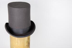 Magic hat. Topper. Elegant vintage gray beige wool felt top hat with black band on the wooden hat block. Grosgrain ribbon trim around rolled brim. Isolated on white background. Close-up. Copy space. photo