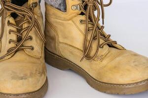 Closeup detail of Pair of worn old yellow hiking trekking lace boots Isolated on white glossy surface with beautiful reflection effect. Second hand tourist walking shoes. Copy Space. White background. photo