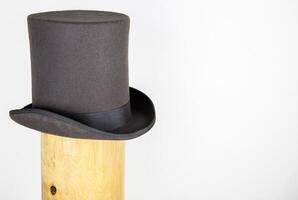 Magic hat. Topper. Elegant vintage gray beige wool felt top hat with black band on the wooden hat block. Grosgrain ribbon trim around rolled brim. Isolated on white background. Close-up. Copy space. photo