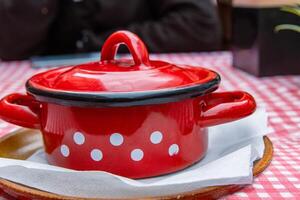 Traditional Slovak Ukrainian Russian cabbage soup with sausage and smoked meat served in retro red metal pot on the plate with spoon. Bowl of delicious Soljanka borsch with white sour cream. Top view photo