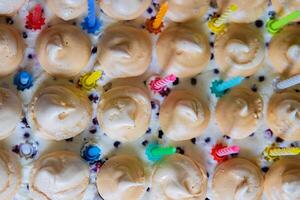 Beautiful Birthday cake with white whipped cream, meringues and cranberries, decorated with multicolored candles. Happy Birthday concept. Pattern for card, poster, banner. Top view. Selective focus photo