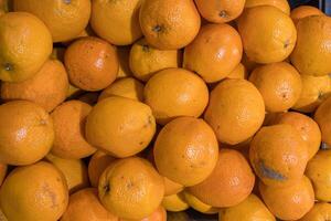 Orange fruits pile on the farmer market counter. Fresh mandarin oranges texture. Top view texture of dirty oranges, market sale. Food market stand. Minimalist, simple concept. Selective focus. photo