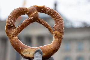 Hand holding Appetizing traditional Bavarian pretzel with the salt crystals. The Berlin Reichstag building can be seen through the bretzel on the blurred background. Symbol of Germany, Bavaria. photo