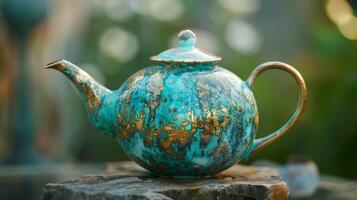 A teapot with a textured crystalline glaze effect in shades of turquoise and gold resembling a piece of gemstone. photo