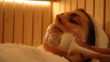 A person sits in a sauna using a silicone brush to apply a gentle chemical peel to their face combining exfoliation with a deep cleanse. photo