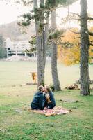 Dad kisses mom with a little boy on her lap while sitting on a blanket in the autumn park photo