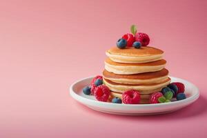 Stack of fluffy pancakes with fresh blueberries and raspberries on a plate against a pink background, ideal for breakfast themes and Shrove Tuesday photo